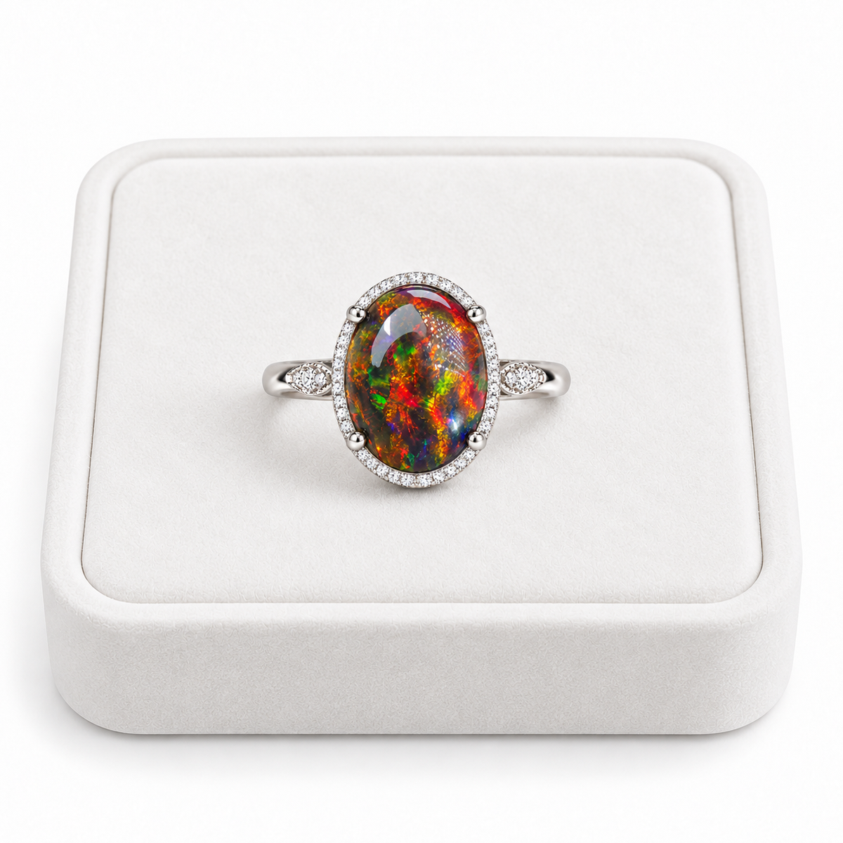 A silver ring with a large oval multicolor opal center stone and a halo of small clear stones, displayed on a white ring box.