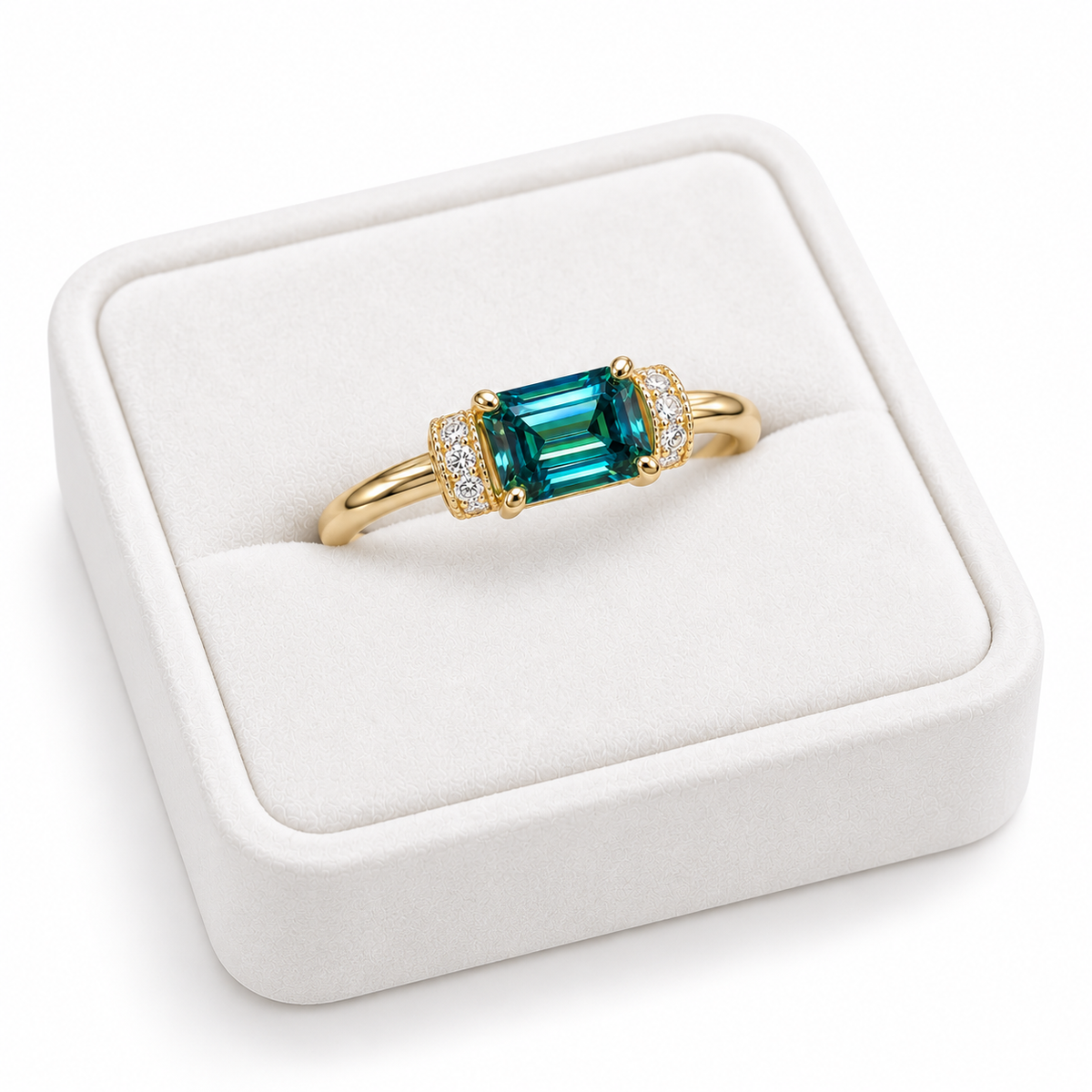 Angled view of a 1 carat green moissanite ring resting on a white velvet jewelry tray, showcasing the elongated 5x7mm emerald-cut gemstone, polished Gold Plated sterling silver band, and decorative cubic zirconia shoulder accents.