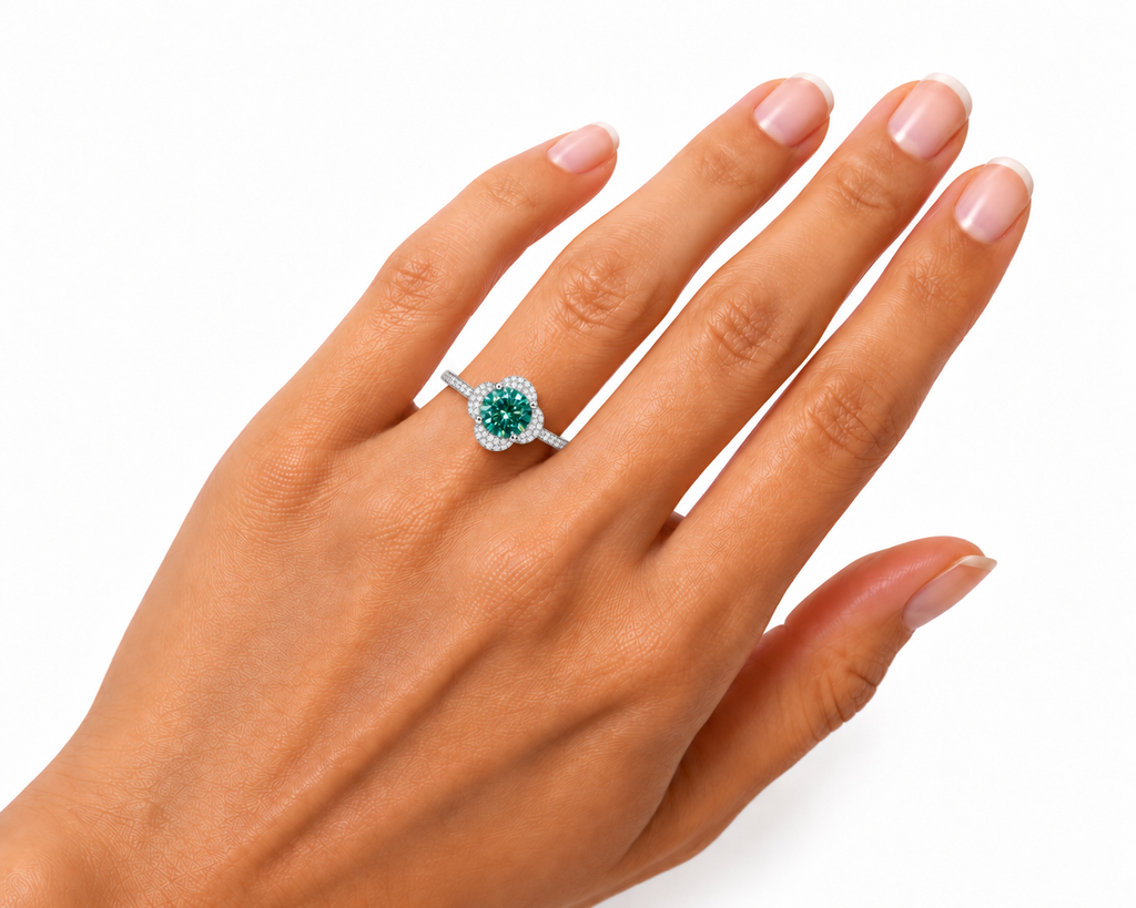 Angled view of a woman's hand wearing a 2 carat round brilliant green moissanite floral halo ring, highlighting the 8mm gemstone's rich emerald-green and teal brilliance, sparkling cubic zirconia flower-inspired setting, and slender sterling silver band.