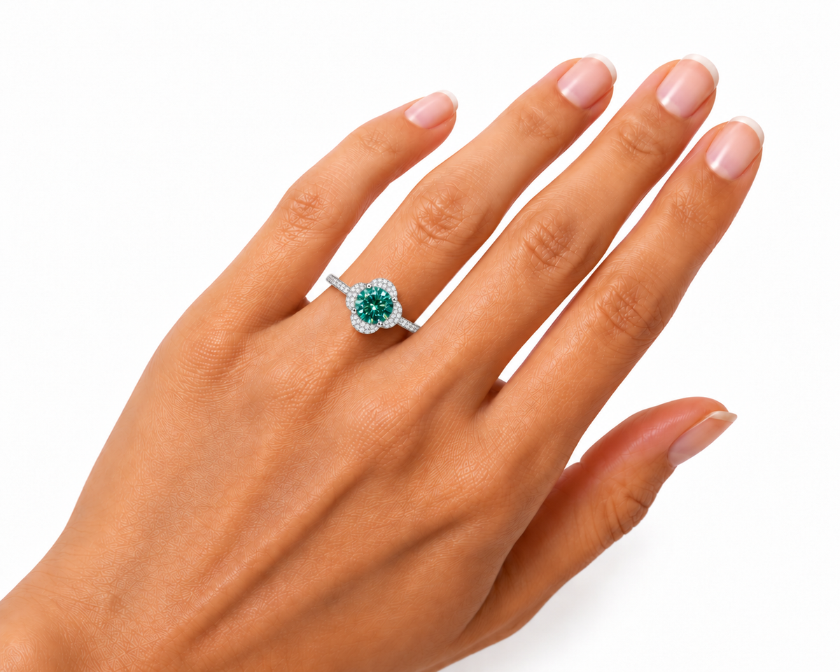Angled view of a woman's hand wearing a 2 carat round brilliant green moissanite floral halo ring, highlighting the 8mm gemstone's rich emerald-green and teal brilliance, sparkling cubic zirconia flower-inspired setting, and slender sterling silver band.