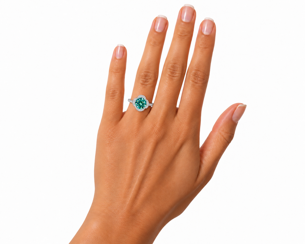 2 carat 8mm round brilliant green moissanite floral halo ring worn naturally on a woman's ring finger, featuring a true-to-size teal-green gemstone, delicate four-petal cubic zirconia halo, and polished sterling silver band against a white background.