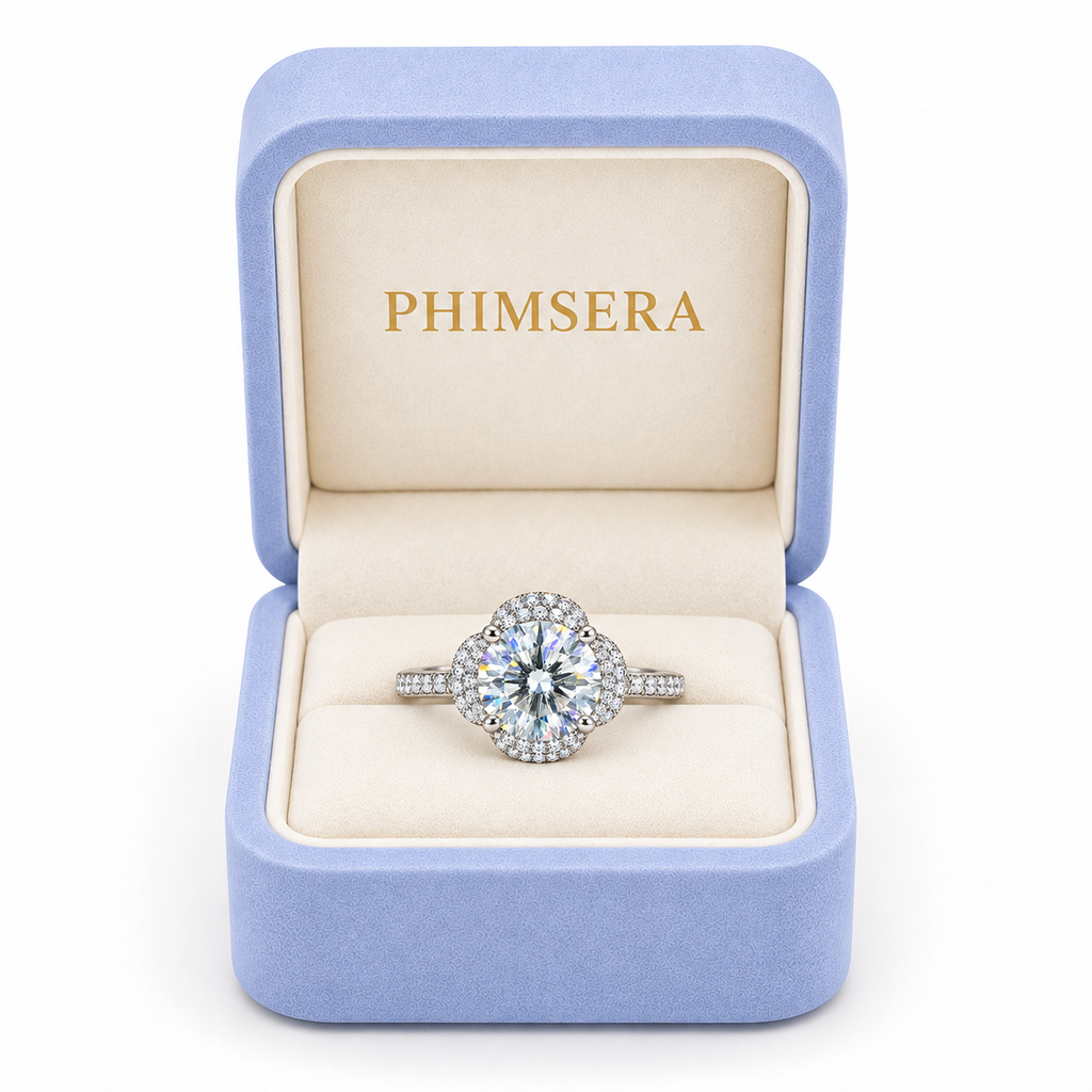 2 carat white moissanite floral halo ring presented inside a periwinkle Phimsera jewelry gift box with ivory interior and gold PHIMSERA lettering against a clean white background.