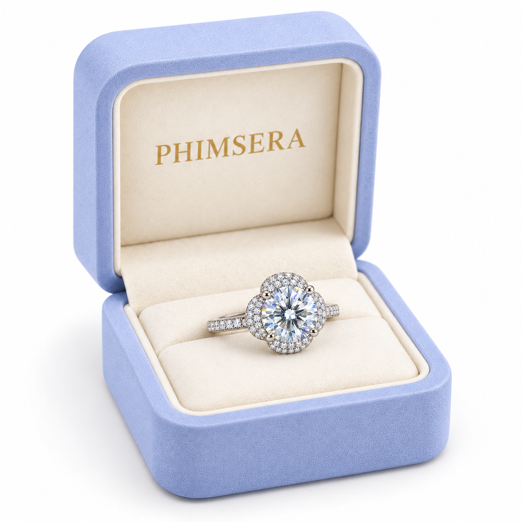 2 carat white moissanite floral halo ring presented inside a periwinkle Phimsera jewelry gift box with ivory interior and gold PHIMSERA lettering against a clean white background.