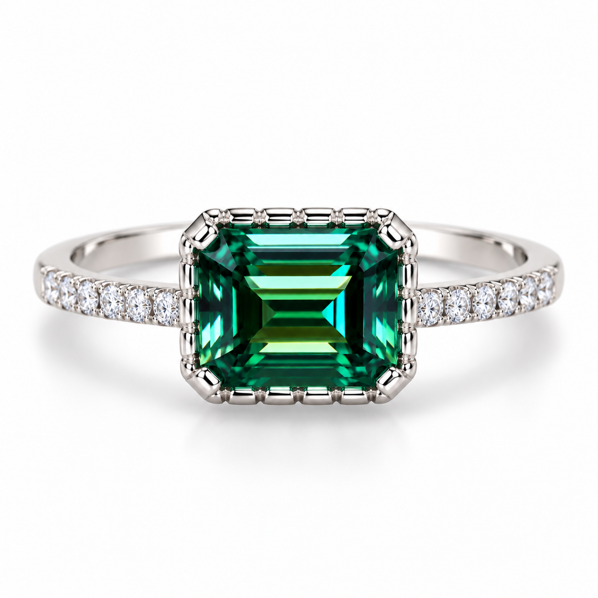 Top-down view of a 6x8mm emerald-cut green moissanite ring showing the elongated horizontal gemstone, deep green and teal step-cut facets, distinctive segmented metal border, and clear cubic zirconia accents along the sterling silver band.