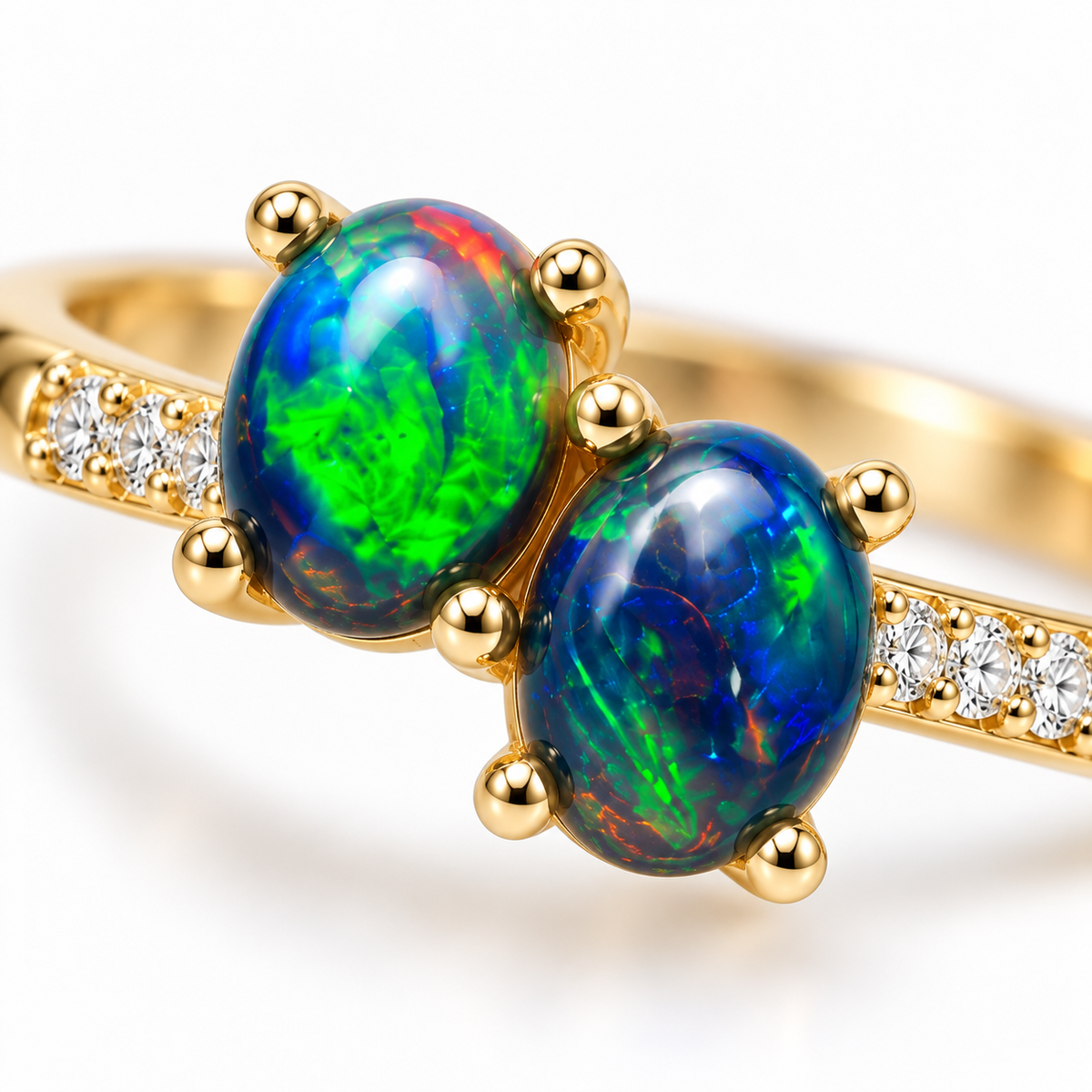 Macro close-up of two 4x5mm oval black fire opals with green, blue and red-orange flashes, surrounded by gold-colored prongs and clear cubic zirconia accents.