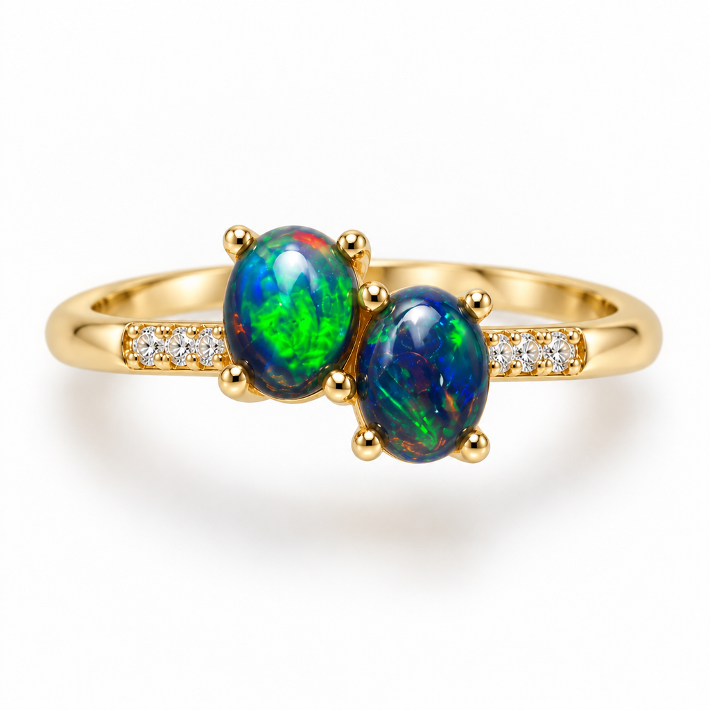 Top view of a black fire opal ring with two 4x5mm oval gemstones displaying vivid blue and green play-of-color, rounded gold-colored prongs, and sparkling cubic zirconia accents.