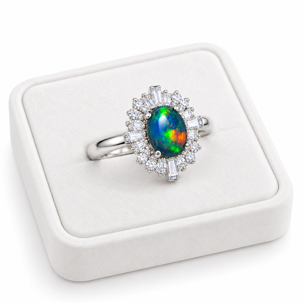 Angled photograph of a black opal halo ring on a white velvet tray, highlighting the colorful oval gemstone and sparkling round and baguette cubic zirconia accents.