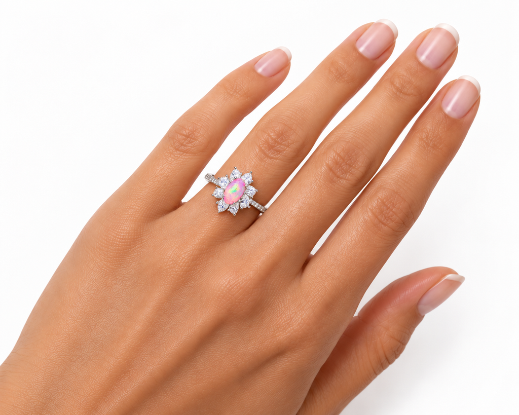 Australian pink fire opal flower ring worn on a woman's ring finger, showing realistic 5x8mm oval gemstone proportions, sparkling pear-shaped cubic zirconia petals, and a slender silver-colored band.