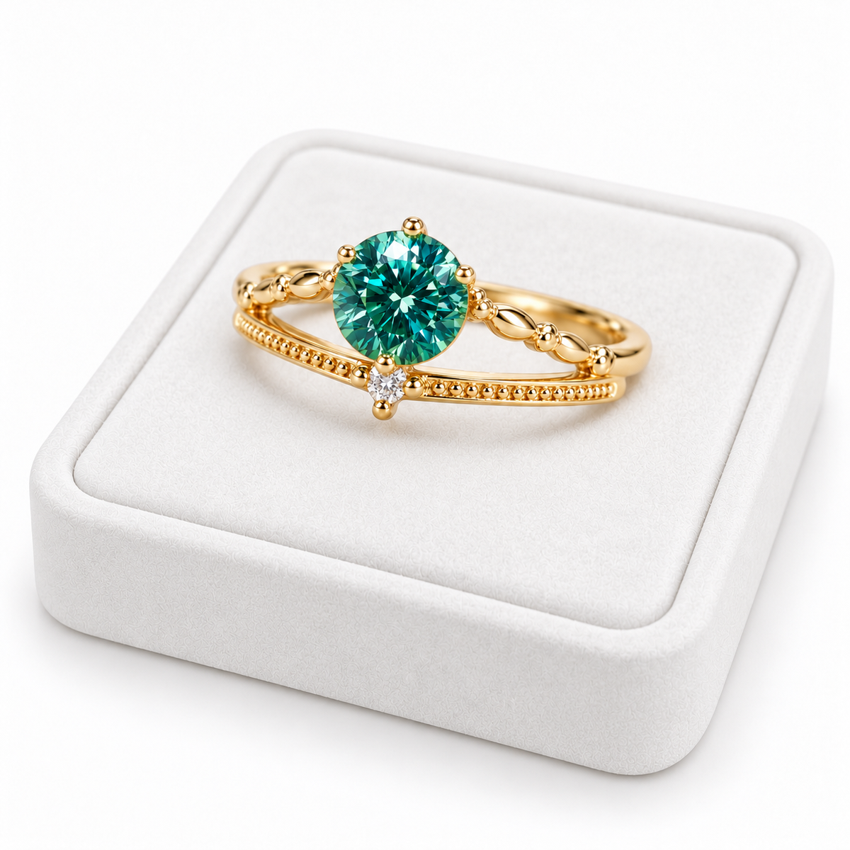 Three-quarter angle photograph of a 6.5mm green moissanite ring resting on a white velvet jewelry tray, showcasing the round brilliant gemstone's rich teal-green reflections, polished four-prong setting, and delicate gold-tone milgrain detailing.