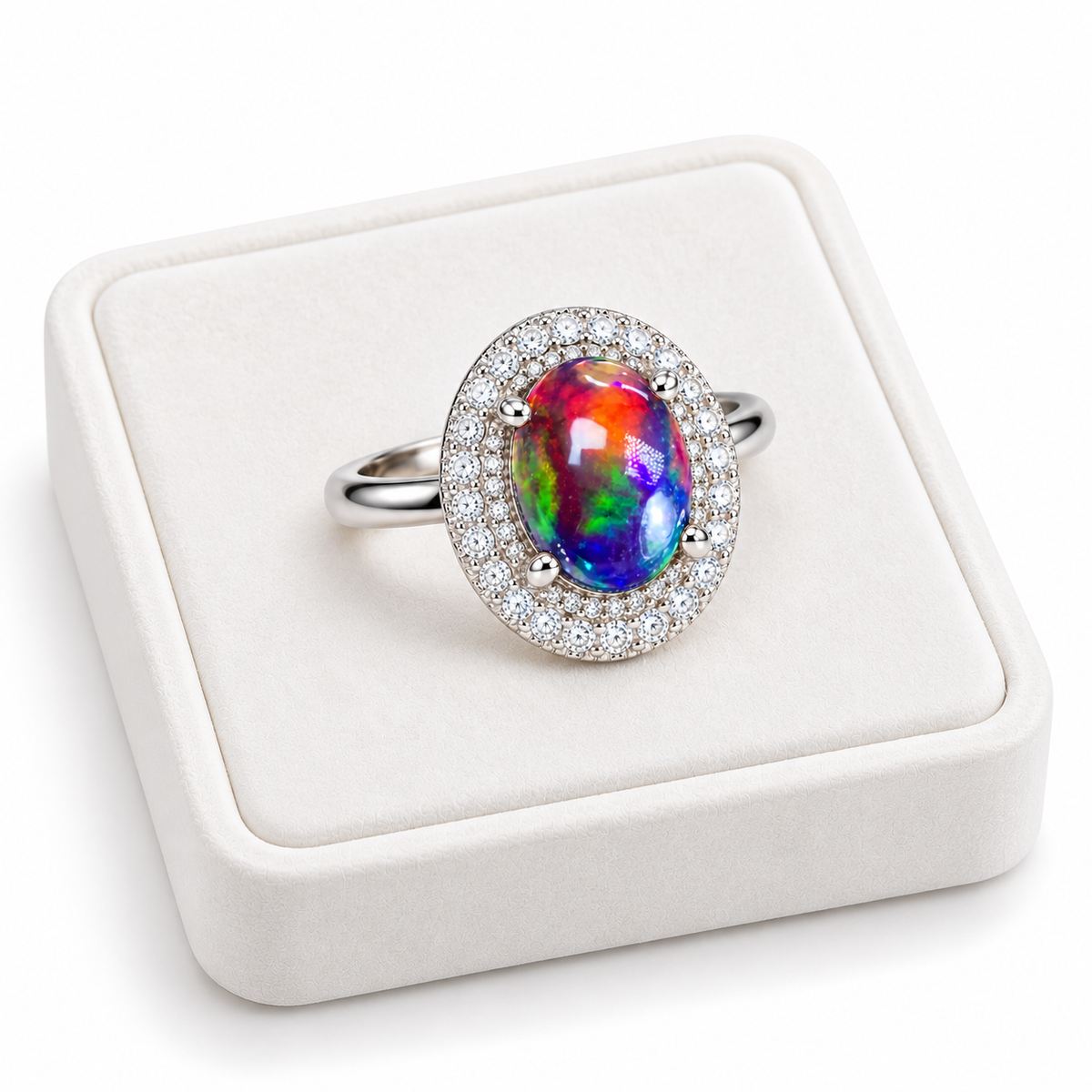 Angled photograph of a 6x8mm Australian black fire opal ring displayed on a white velvet tray, highlighting the colorful opal and sparkling cubic zirconia double halo.