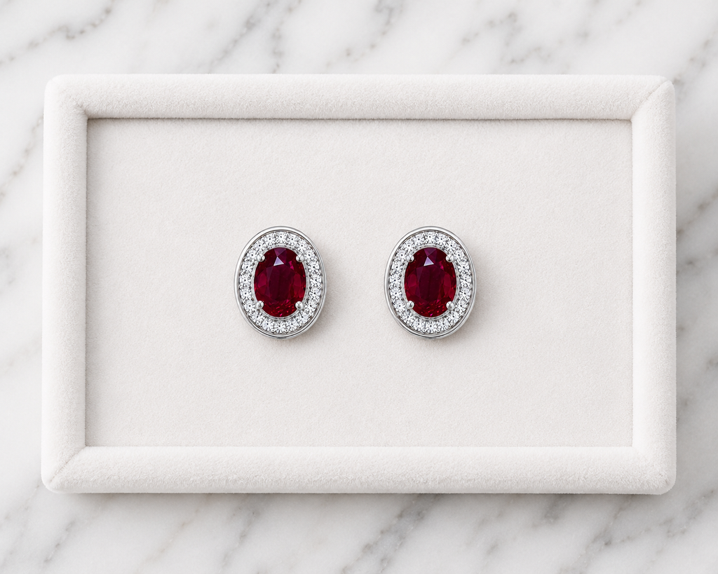 Natural 4x6mm oval ruby halo stud earrings in platinum plated 925 sterling silver with sparkling cubic zirconia on a white background.
