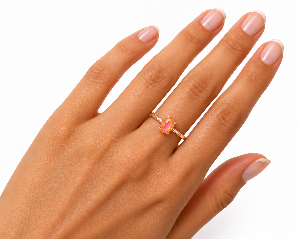A close-up of a hand wearing a delicate rose gold ring with a marquise-cut pink gemstone, set against a clean white background.