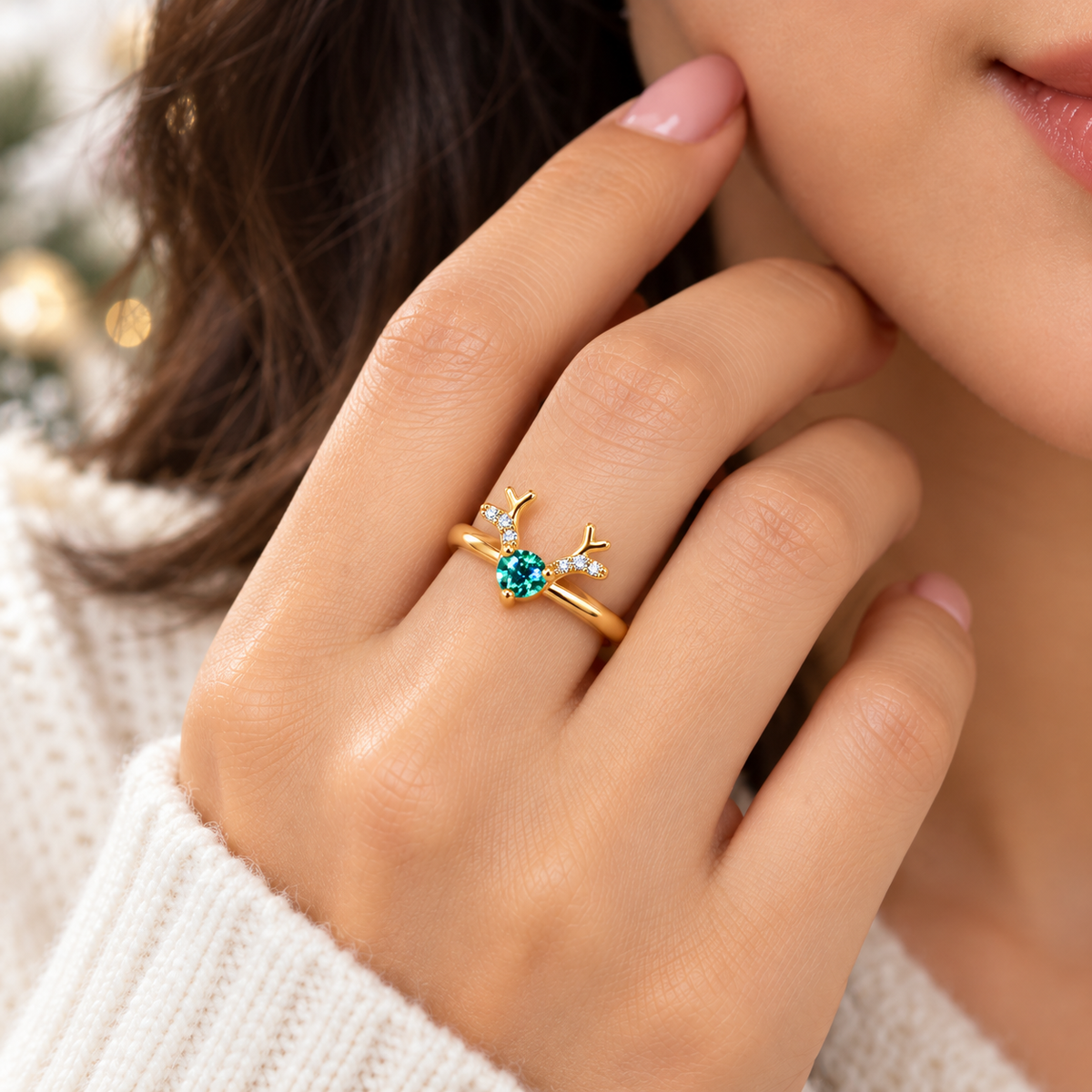 A close-up lifestyle shot of a woman's hand wearing a gold ring with a central round-cut blue gemstone and two small clear accent stones forming a leaf design.