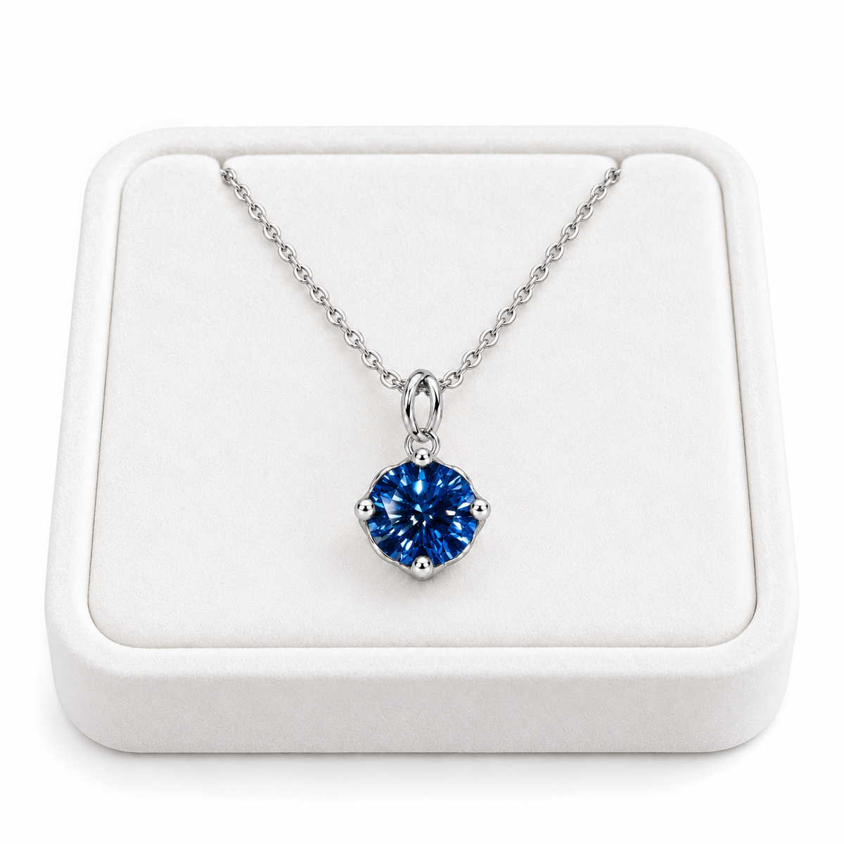 2 carat deep blue moissanite solitaire necklace arranged on a premium white velvet jewelry tray with a delicate sterling silver chain and brilliant 8mm royal-blue round gemstone against a pure white background.