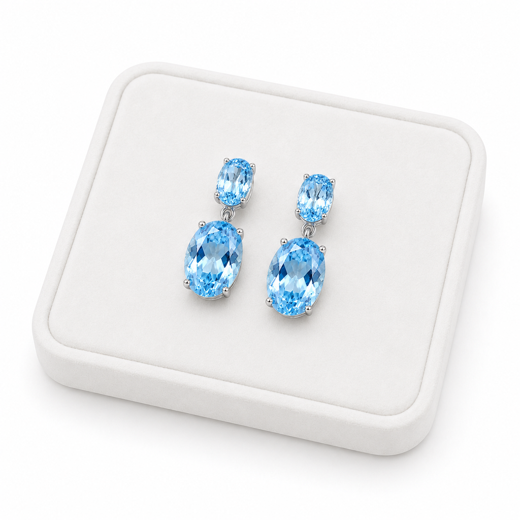Natural Sky Blue Topaz drop earrings with 4x6mm and 8x10mm oval gemstones on a white tray