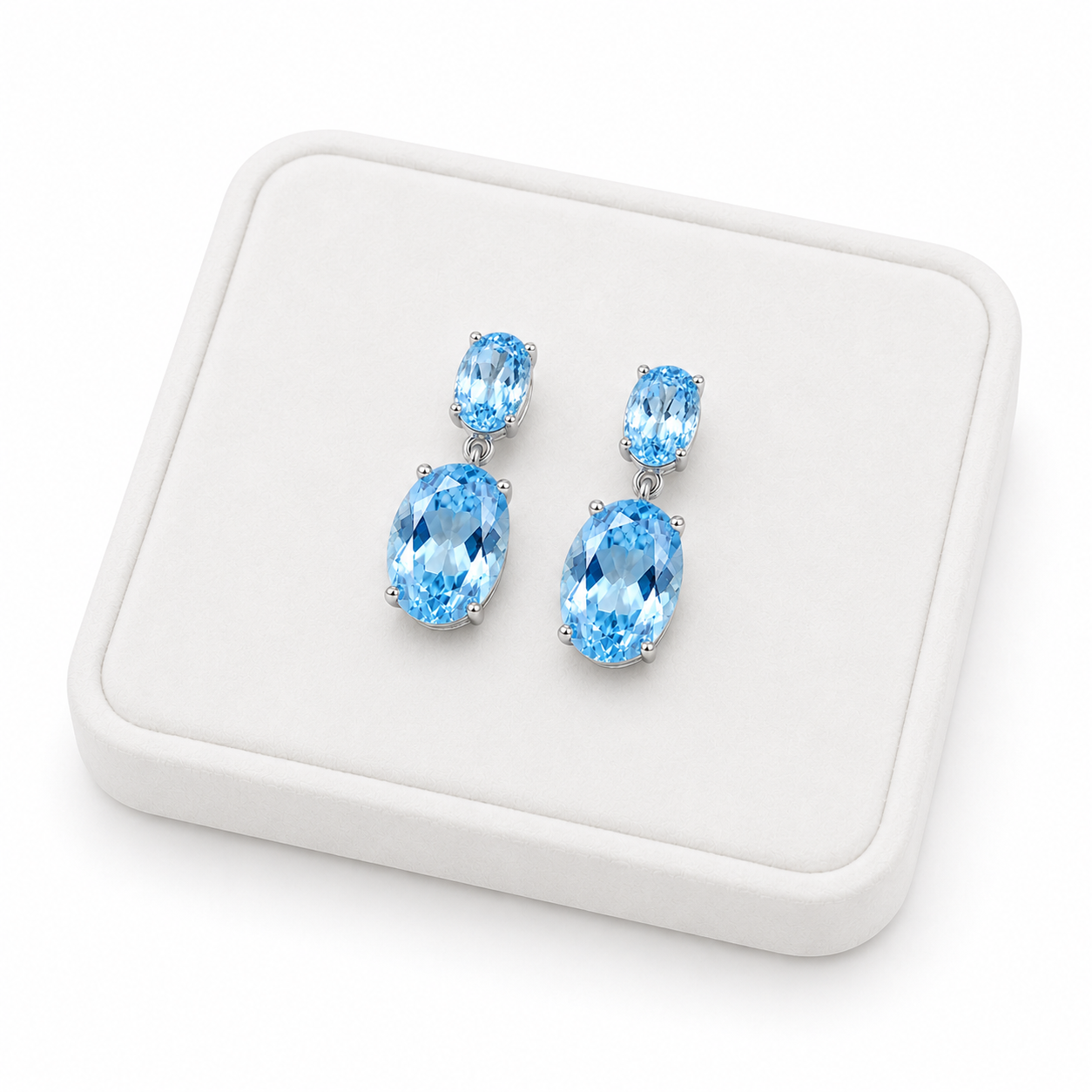 Natural Sky Blue Topaz drop earrings with 4x6mm and 8x10mm oval gemstones on a white tray