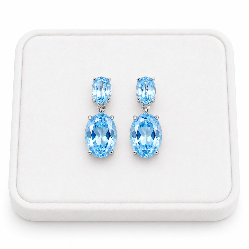 Natural Sky Blue Topaz drop earrings with 4x6mm and 8x10mm oval gemstones on a white tray