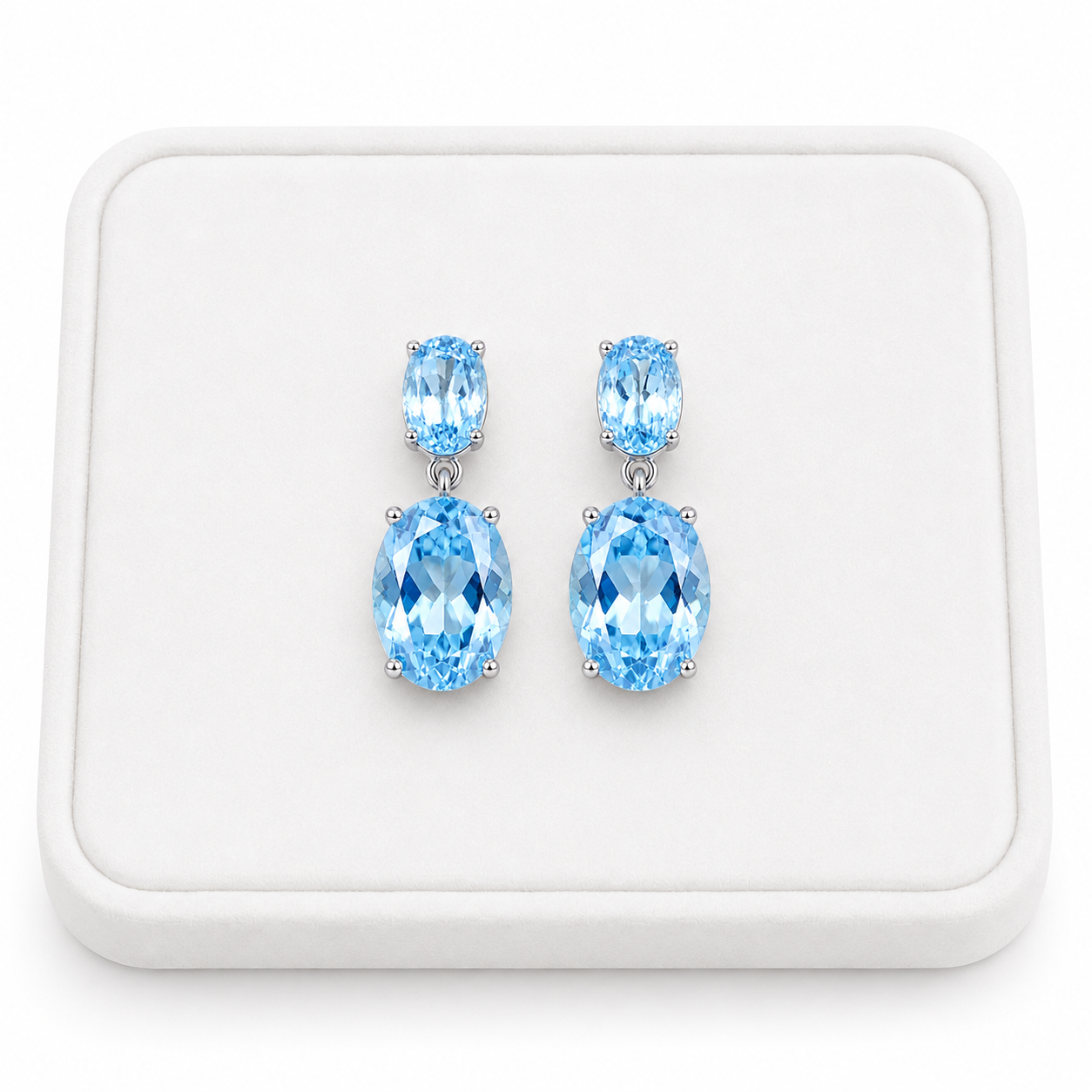 Natural Sky Blue Topaz drop earrings with 4x6mm and 8x10mm oval gemstones on a white tray