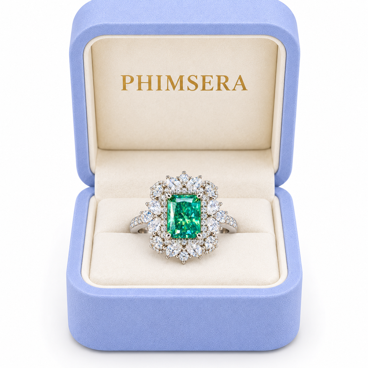 A PHIMSERA brand emerald-cut green gemstone ring with a diamond halo, presented in an open light blue velvet jewelry box with a cream interior.