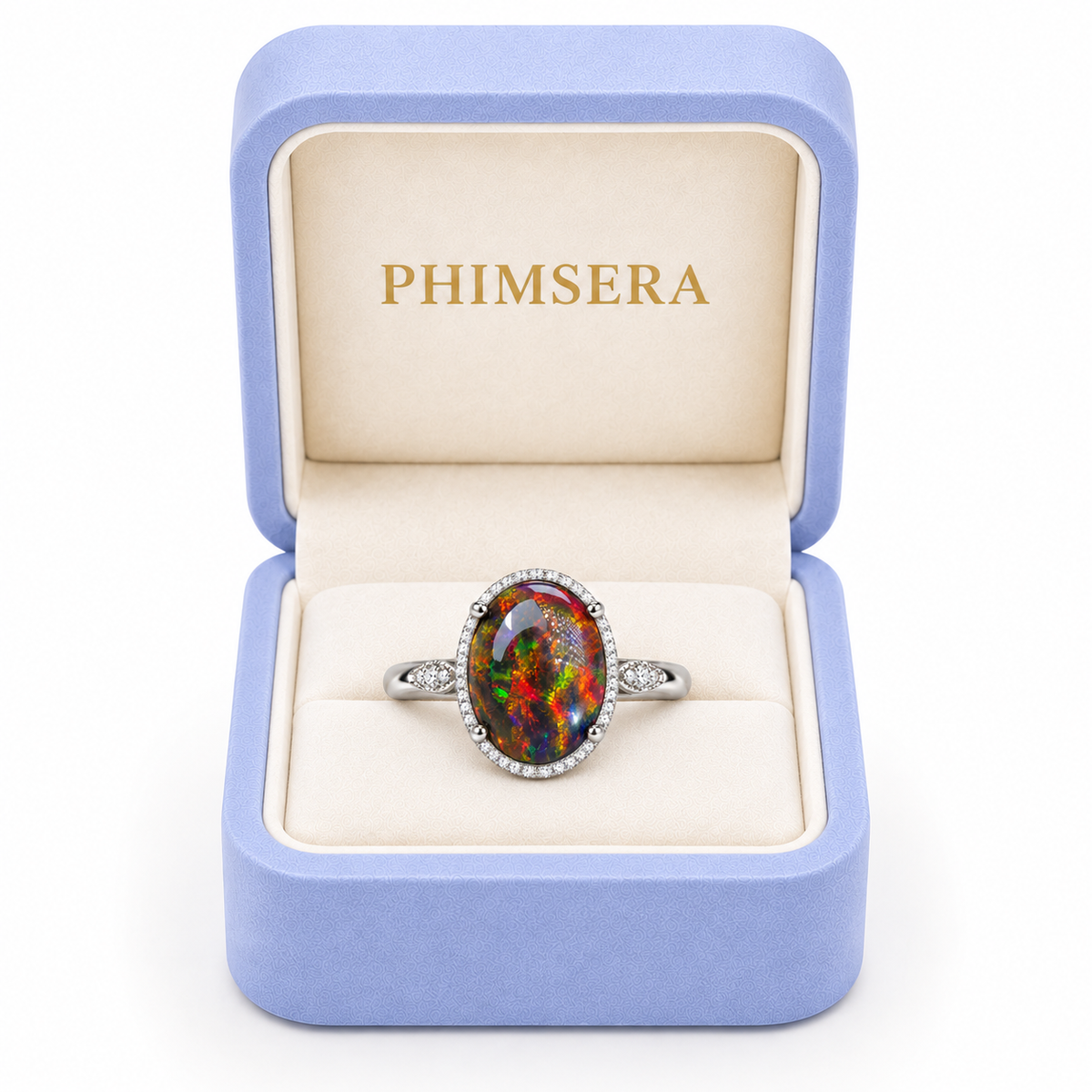 10x14mm black fire opal ring with vivid multicolor flashes, four prongs, and a sparkling halo presented in an open periwinkle Phimsera jewelry box with cream velvet lining.