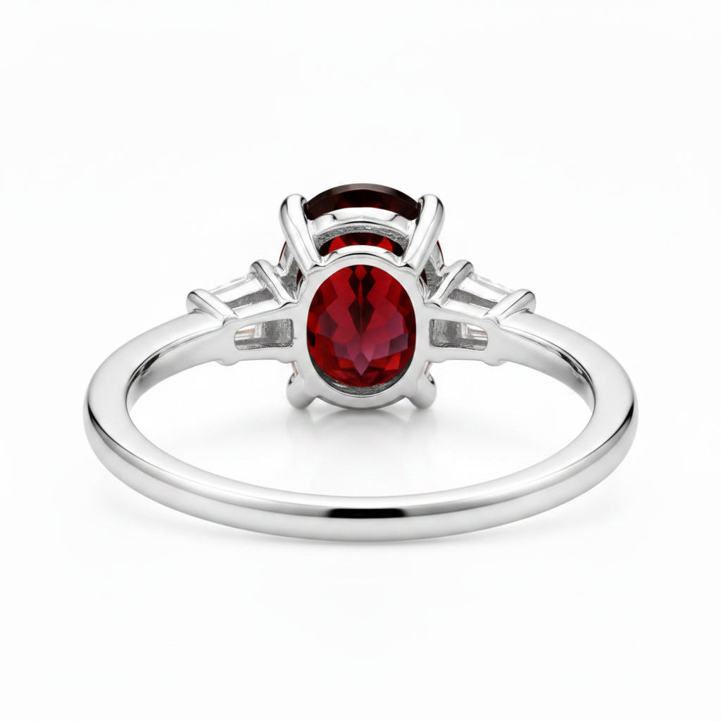 Natural 7x9mm oval red garnet solitaire ring with tapered cubic zirconia accent stones in sterling silver.