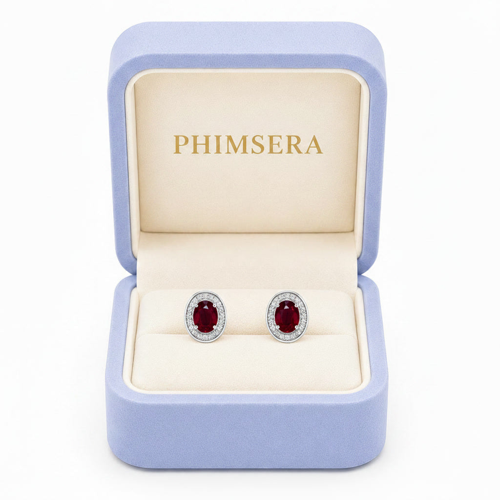 Natural 4x6mm oval ruby halo stud earrings in platinum plated 925 sterling silver with sparkling cubic zirconia on a white background.