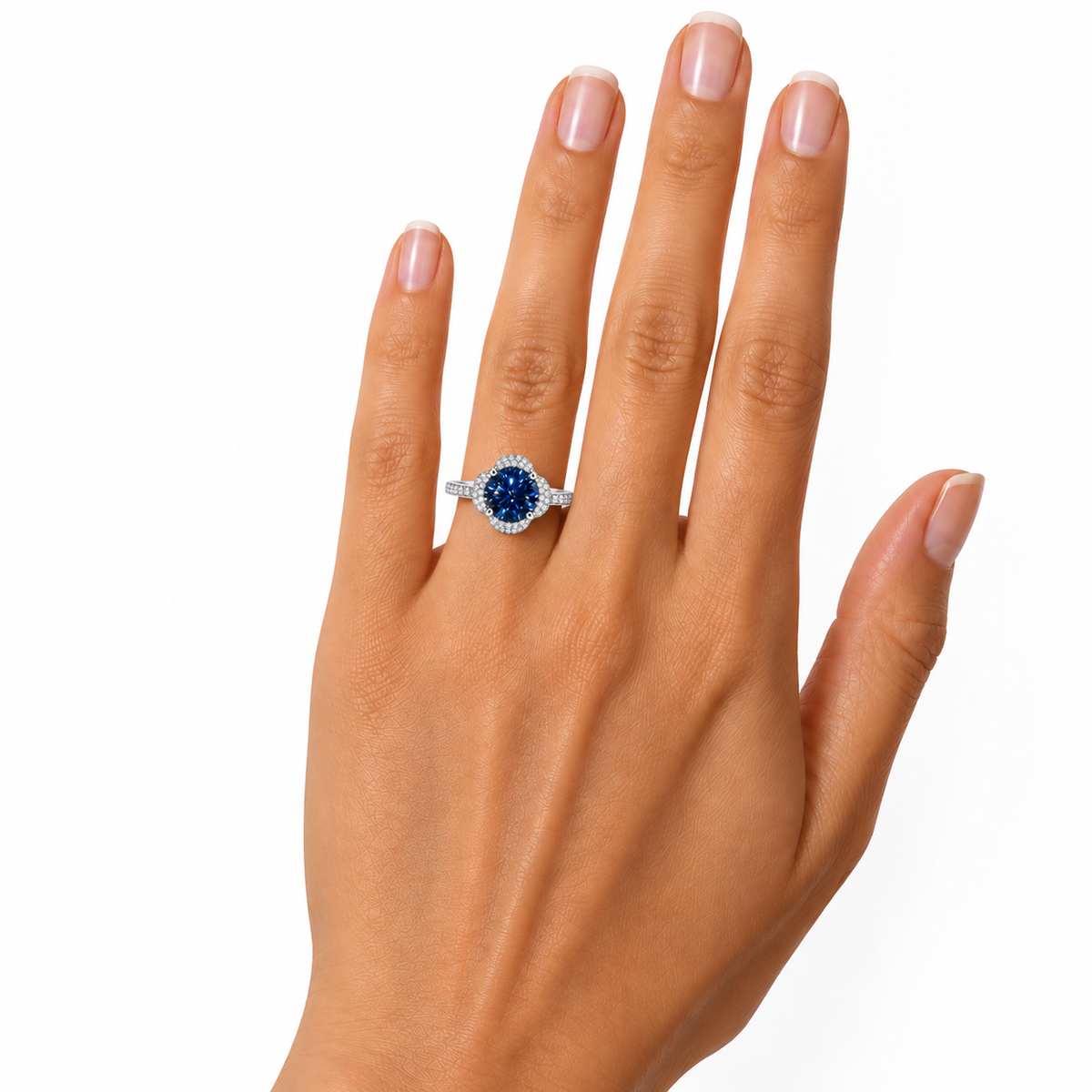 Alternate hand model photograph of a 2 carat royal blue moissanite floral halo ring on a woman's ring finger, showcasing its elegant proportions and delicate pavé band against white.
