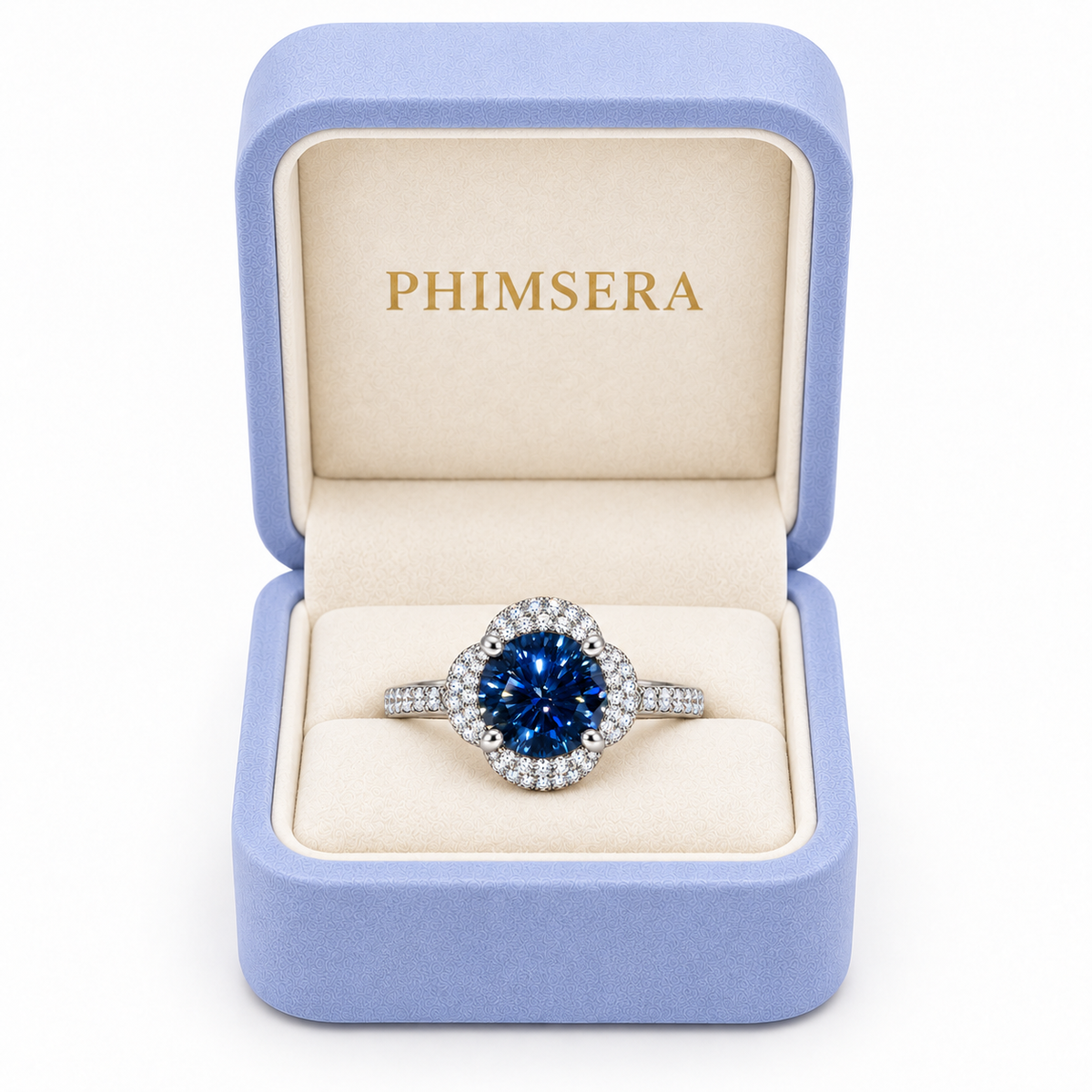 Deep blue moissanite floral halo ring presented inside a periwinkle Phimsera jewelry gift box with ivory interior and gold PHIMSERA lettering against a pure white background.