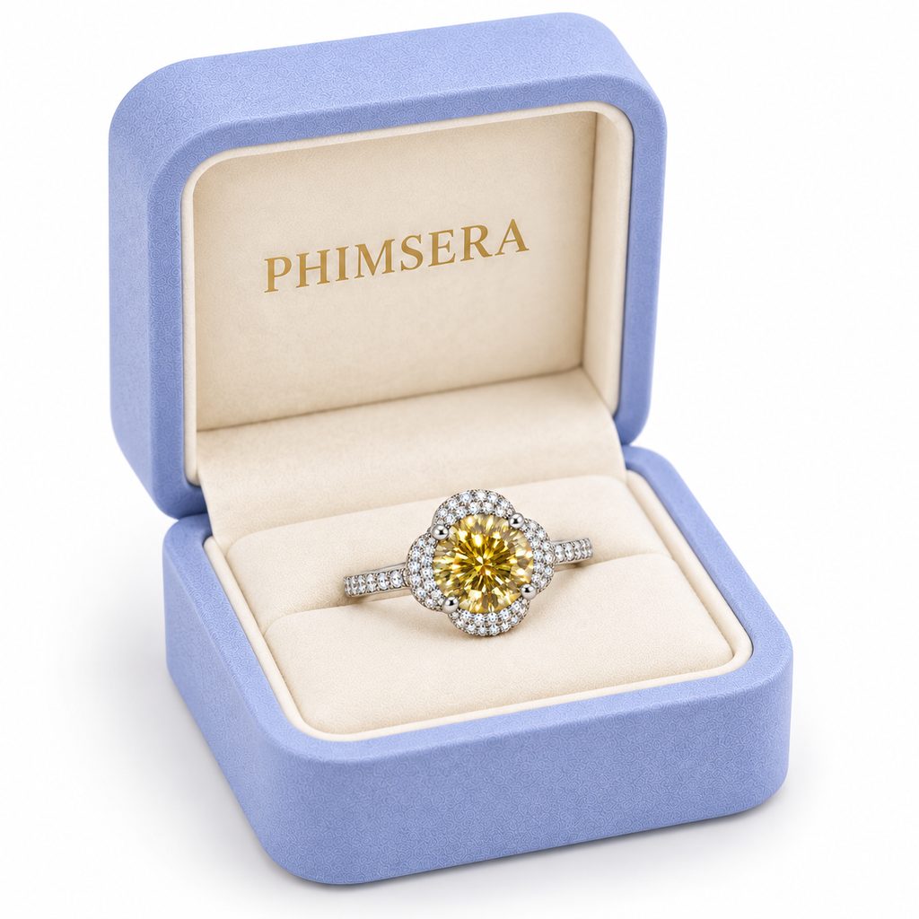 Three-quarter view of a 2 carat yellow moissanite floral halo ring presented in a slightly turned periwinkle Phimsera jewelry box with cream lining and gold branding.