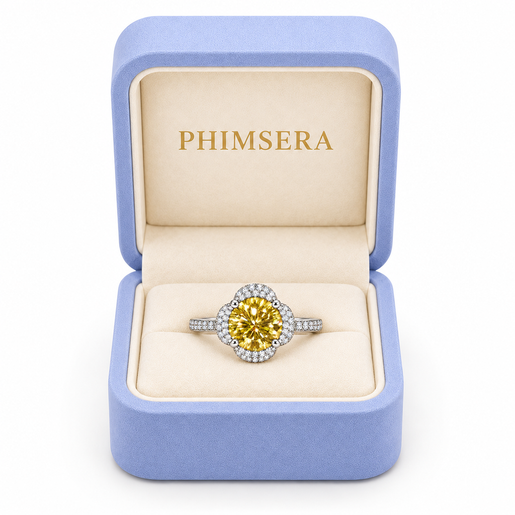 Brilliant yellow moissanite floral halo ring displayed inside a periwinkle Phimsera jewelry gift box with ivory velvet interior and gold PHIMSERA lettering against white.