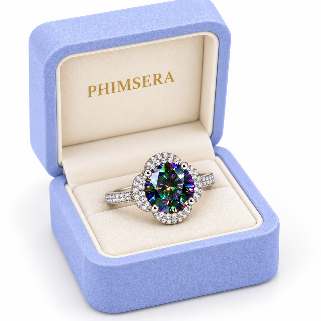 Three-quarter view of a 2 carat black rainbow moissanite floral halo ring presented in a slightly turned periwinkle Phimsera jewelry box with cream velvet lining, gold branding and a pure white background.