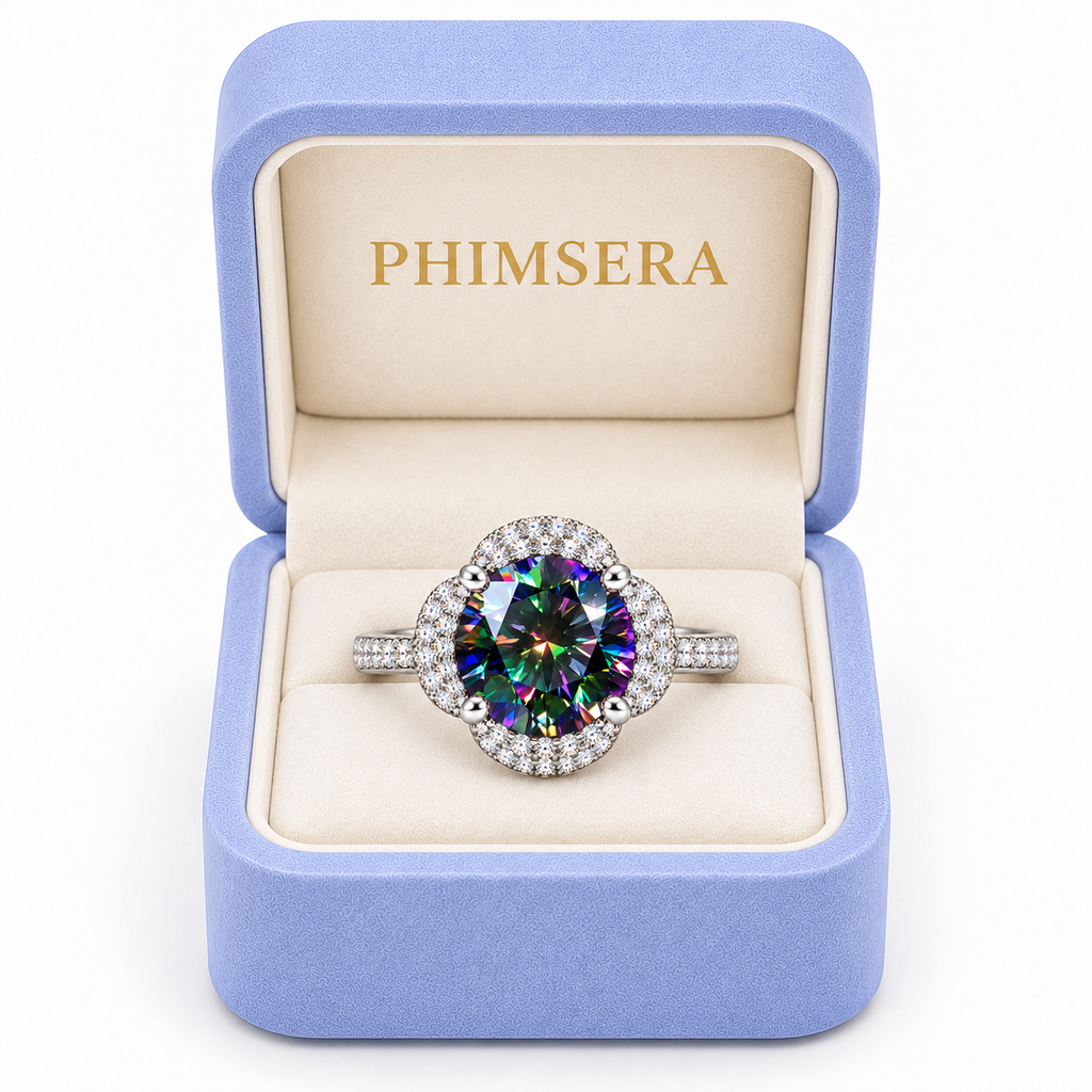 Black rainbow moissanite floral halo ring displayed inside a periwinkle Phimsera jewelry gift box with ivory velvet interior and gold PHIMSERA lettering, featuring a vibrant multicolored gemstone and sparkling sterling silver setting.