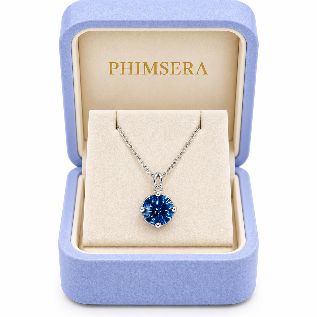 2 carat deep blue moissanite solitaire necklace displayed inside an open periwinkle Phimsera jewelry gift box with an ivory interior, gold Phimsera logo, and white studio background.