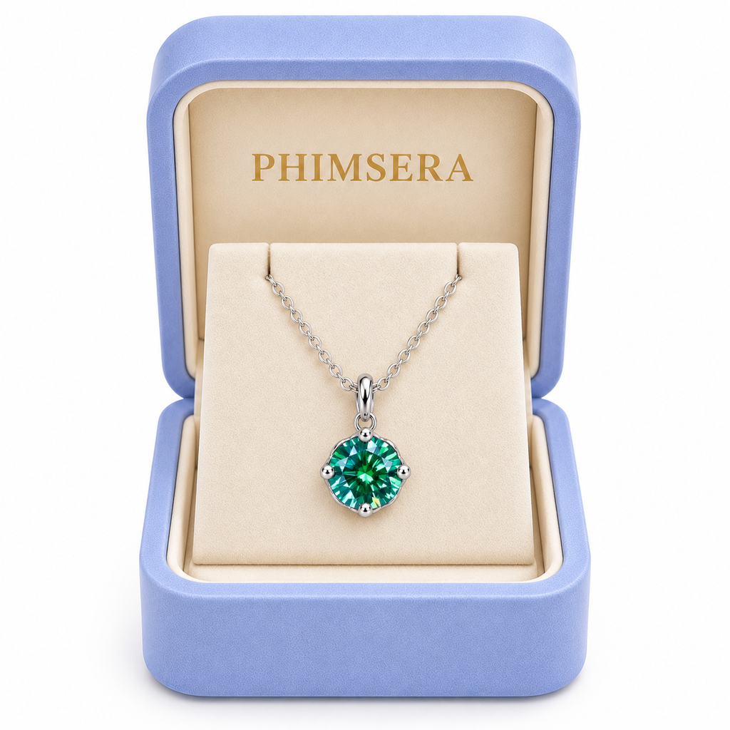 2 carat emerald green moissanite solitaire necklace displayed inside an open periwinkle Phimsera jewelry gift box with an ivory interior, gold Phimsera logo, and white studio background.