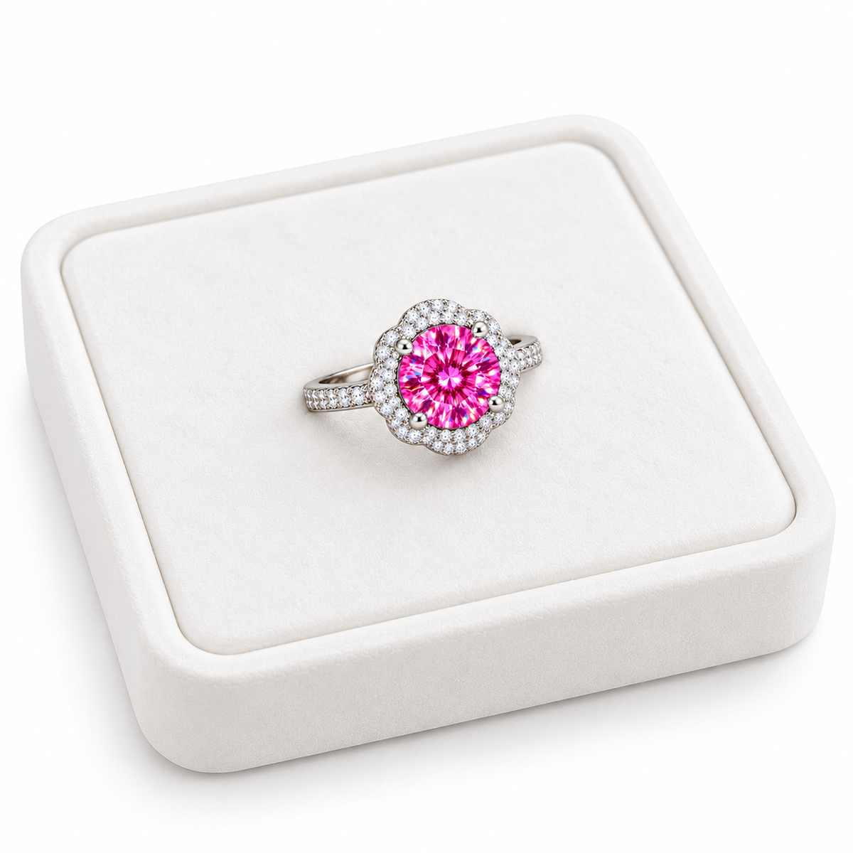Angled view of an 8mm pink moissanite floral halo ring resting on a slightly turned white velvet jewelry tray, showcasing the brilliant pink gemstone, delicate four-petal halo and pavé sterling silver band.