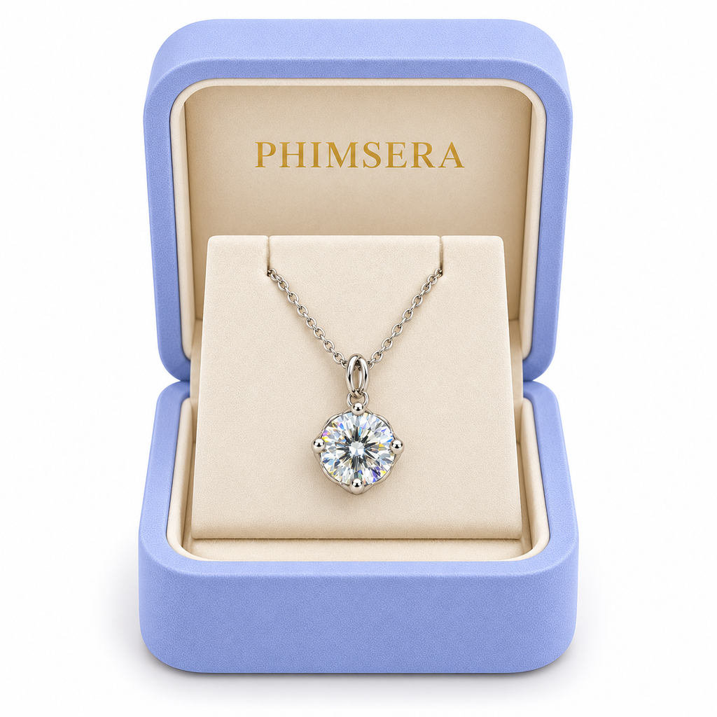 2 carat white moissanite solitaire necklace displayed inside an open periwinkle Phimsera jewelry gift box with an ivory interior, gold Phimsera logo, and white background.