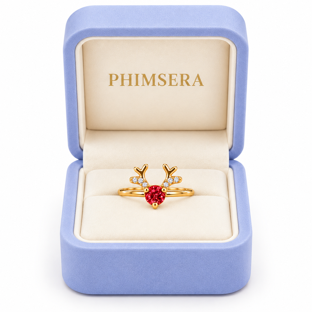 Phimsera 4mm red moissanite Christmas reindeer ring displayed inside an open periwinkle jewelry gift box with an ivory interior and gold Phimsera branding against a white background.