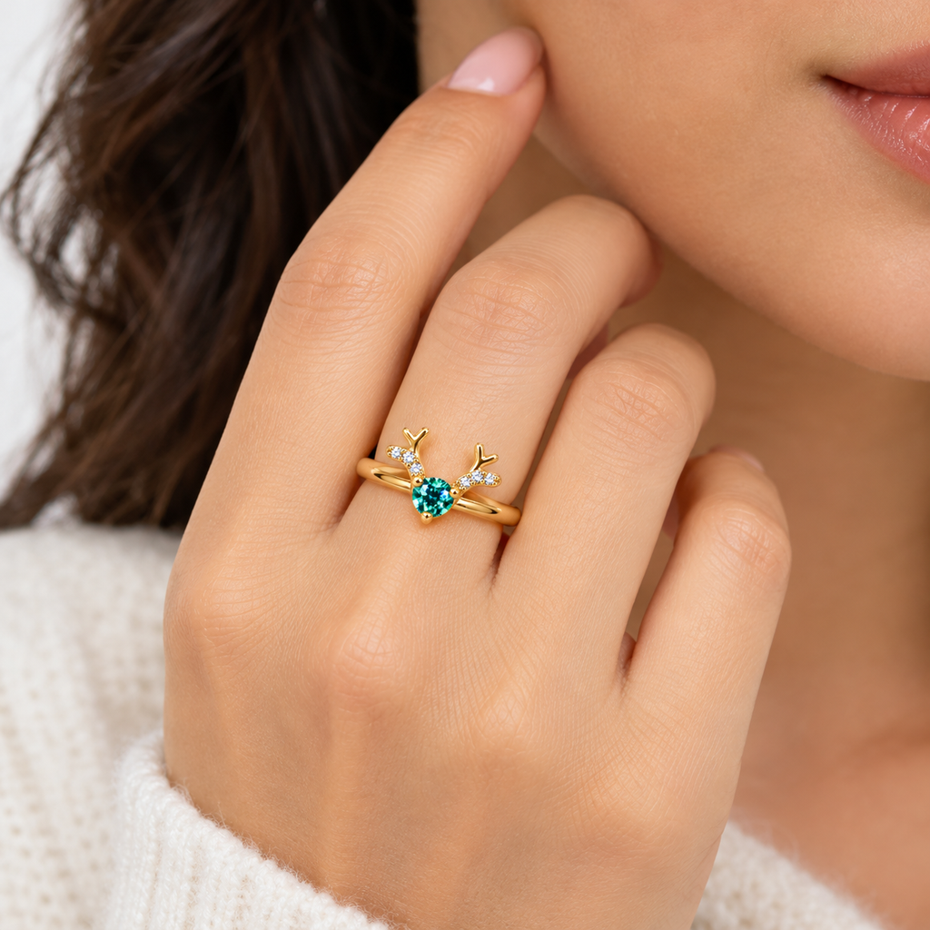 Gold-plated Christmas reindeer antler ring worn on a woman's ring finger, featuring a true-to-size 4mm round green moissanite gemstone and sparkling cubic zirconia antler accents.