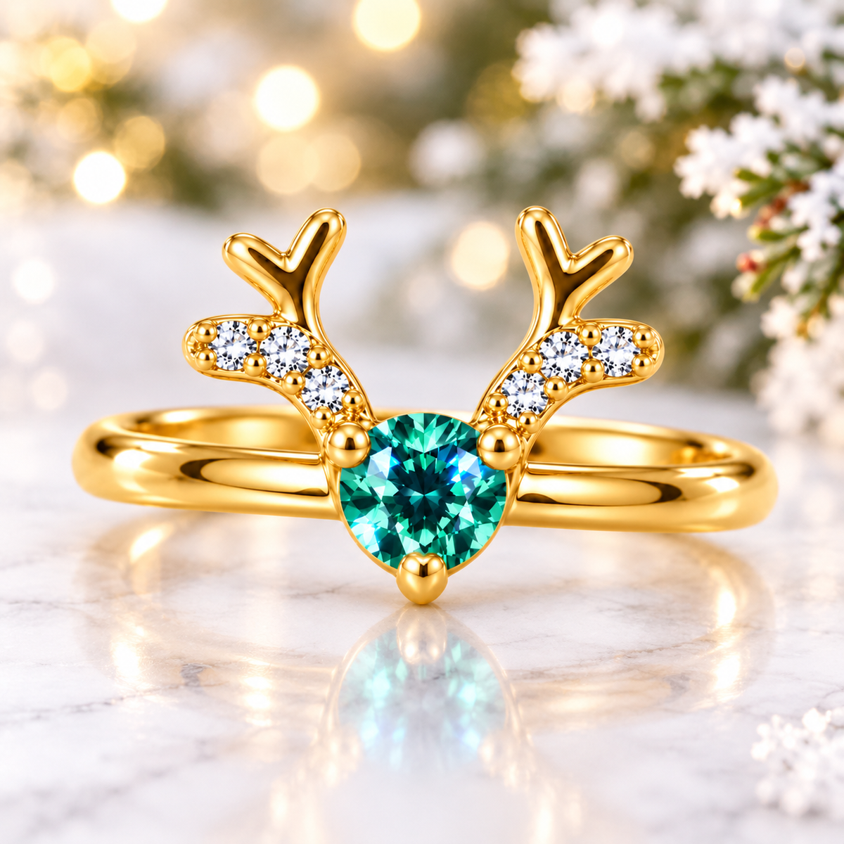 Front view of a gold Christmas reindeer antler ring with a brilliant teal-green moissanite gemstone resting on white snow among frosted pine branches and warm holiday lights.