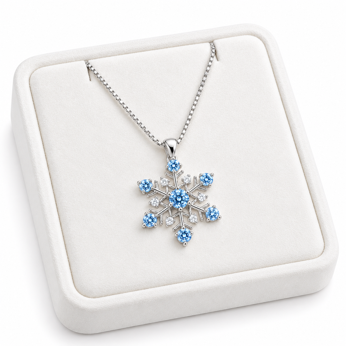 Angled presentation of an icy blue moissanite snowflake pendant necklace on a slightly turned white velvet jewelry tray, highlighting the delicate silver chain, brilliant blue gemstones and intricate six-point snowflake setting.