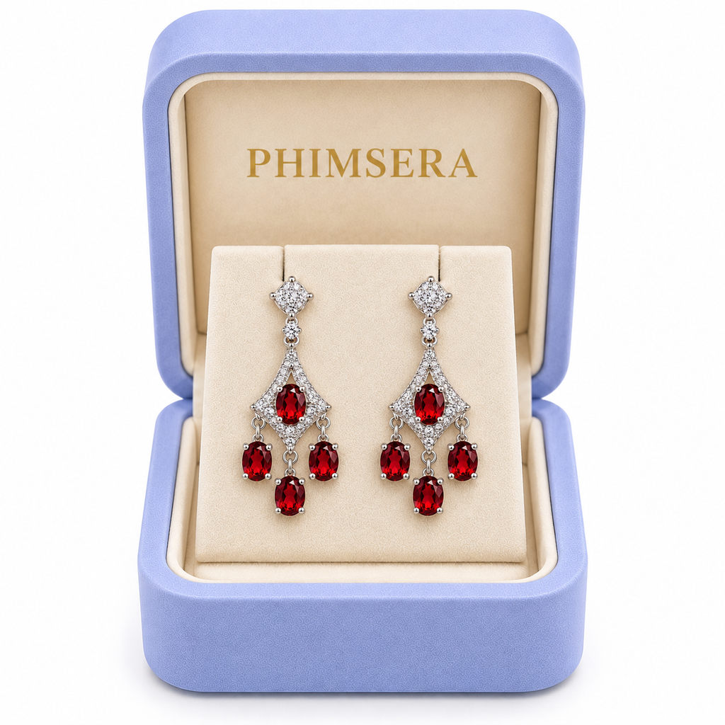 Natural red garnet chandelier dangle earrings displayed inside an open periwinkle Phimsera jewelry gift box with an ivory interior and gold Phimsera logo, featuring sparkling cubic zirconia accents and cascading 4x5mm crimson-red garnet gemstones against a pure white background.