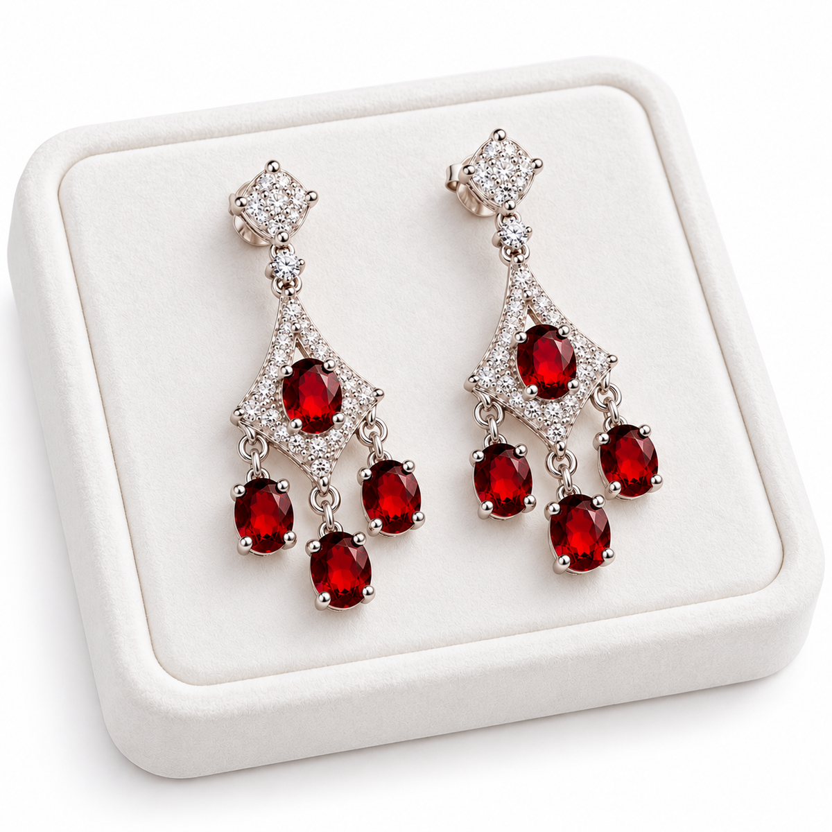 Angled white velvet jewelry tray displaying matching natural red garnet chandelier earrings with oval 4x5mm gemstones, sparkling cubic zirconia geometric frames, polished sterling silver settings, and cascading crimson-red gemstone drops.