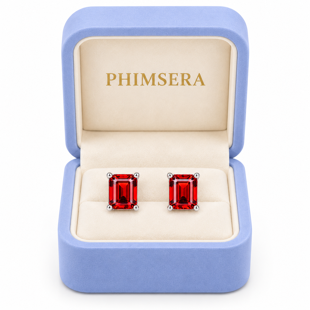 Natural 6x8mm red garnet emerald cut stud earrings displayed inside an open periwinkle Phimsera jewelry gift box with an ivory interior, gold Phimsera logo, and pure white background.