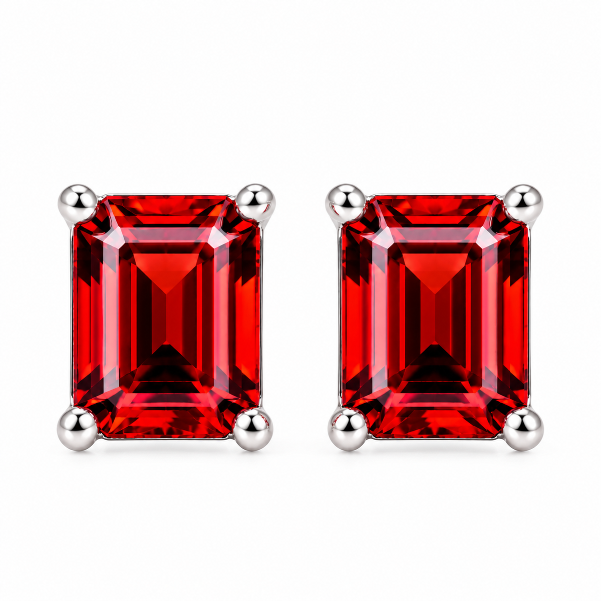 Top-down photograph of matching natural red garnet emerald cut stud earrings with 6x8mm rectangular gemstones, symmetrical four-prong sterling silver settings, and deep crimson-red reflections against a pure white background.