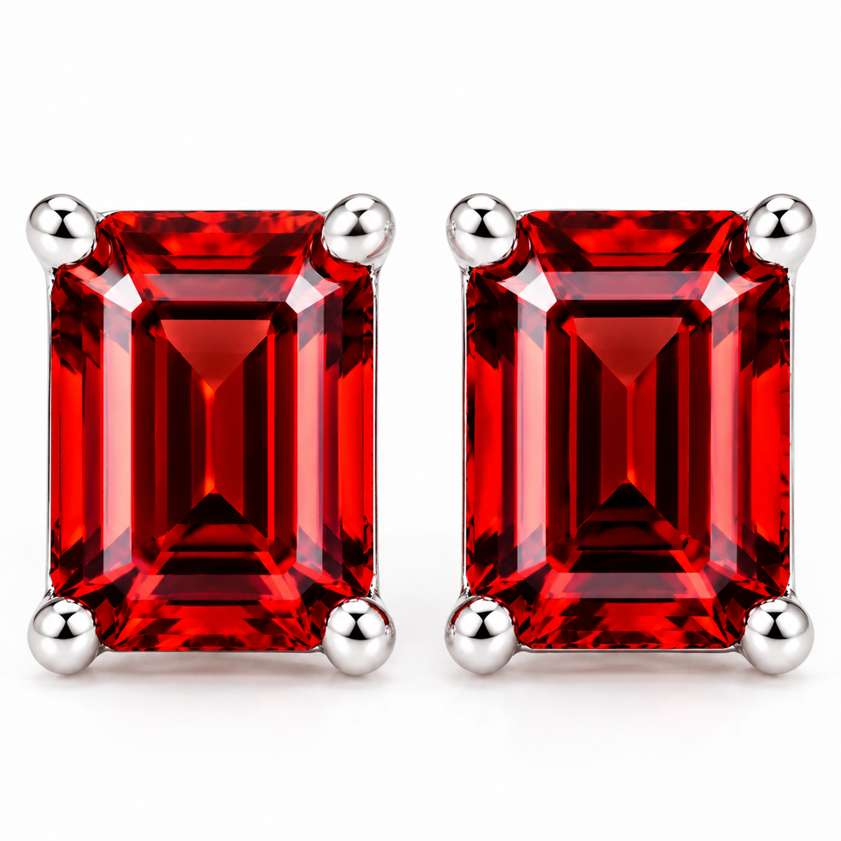 Extreme frontal macro of natural red garnet emerald cut stud earrings featuring 6x8mm rectangular gemstones with rich crimson-red step-cut facets and polished sterling silver four-prong settings on a white background.