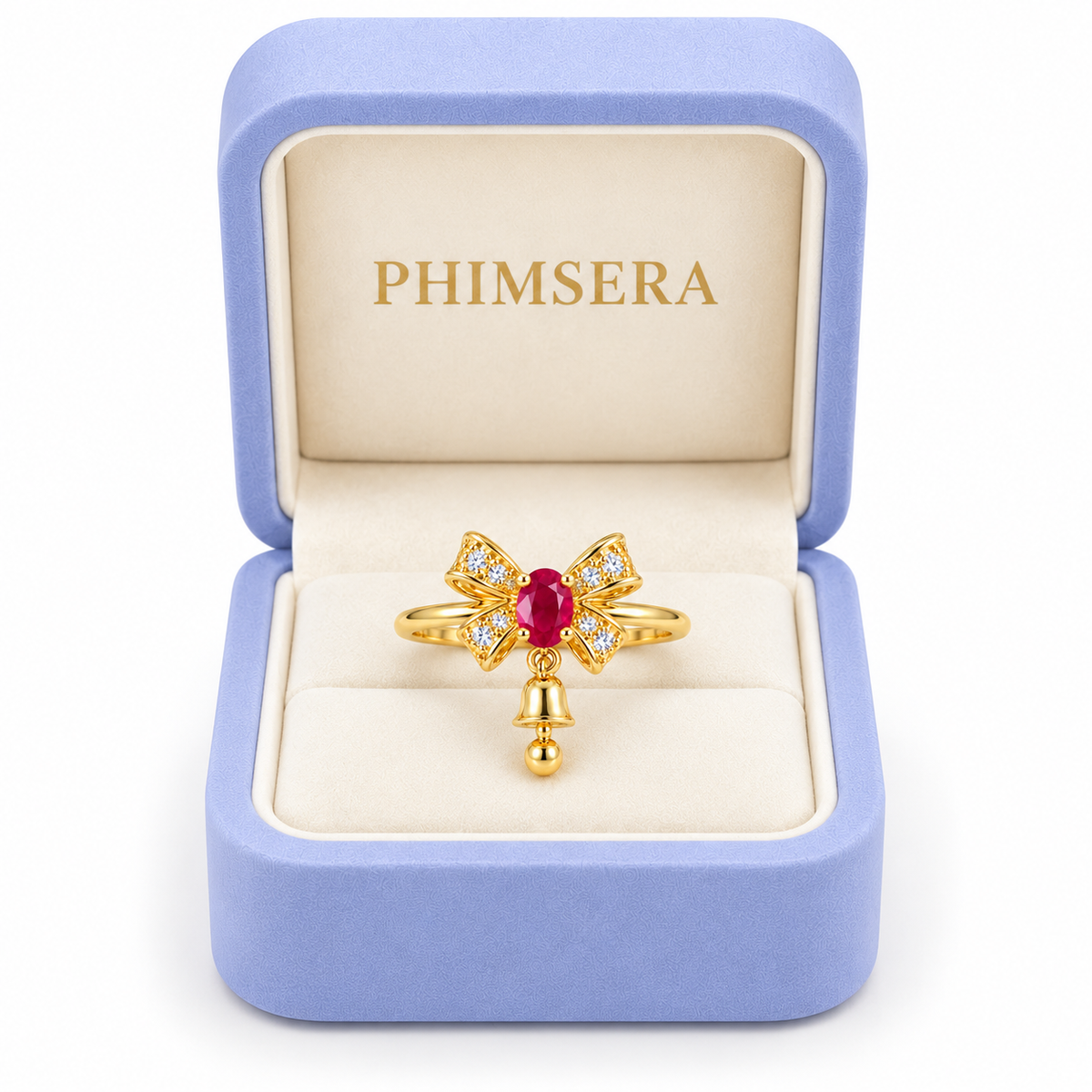 Natural ruby Christmas bow ring with a petite dangling gold bell displayed inside an open periwinkle Phimsera jewelry gift box with an ivory interior and gold PHIMSERA logo against a white background.