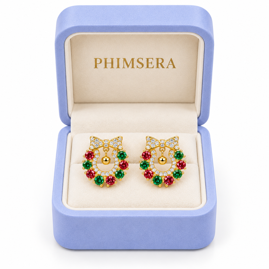 Red and green moissanite Christmas wreath earrings displayed inside an open periwinkle Phimsera jewelry gift box with an ivory interior and gold PHIMSERA lettering against a white background.