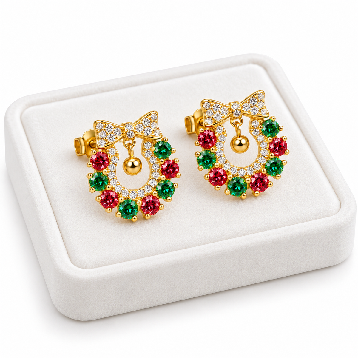 Angled white velvet tray presentation of Christmas wreath earrings featuring alternating ruby-red and emerald-green moissanite gemstones, sparkling white cubic zirconia and gold ornament charms.