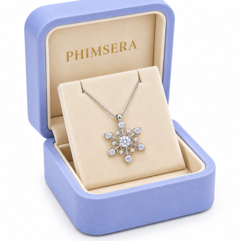 Three-quarter view of a white moissanite snowflake pendant necklace presented in an open periwinkle Phimsera jewelry box with cream velvet lining and elegant gold branding against a white background.